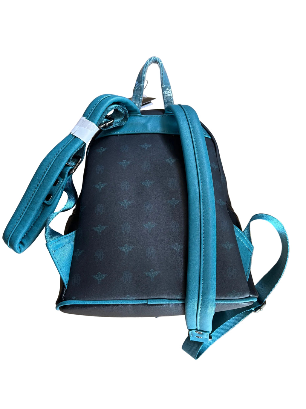 Haunted Mansion Backpack. A small backpack with a black and teal monogram pattern, photographed from above on a wooden floor. The backpack has teal straps and trim, and a white tag is attached near the top handle.